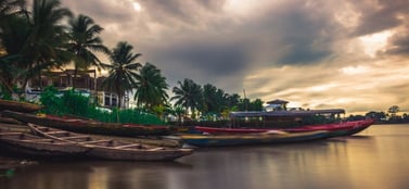 Traditional wooden boats resting on a riverbank in Cameroon at sunset with palm trees in the background, representing the foundational and diverse range of business entities available in the region.