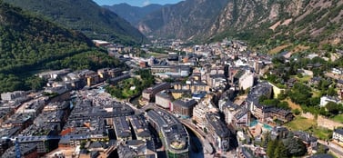 An aerial view of the modern urban buildings of Andorra la Vella nestled within a steep green mountain valley, representing the strategic and established range of business entities in the region.