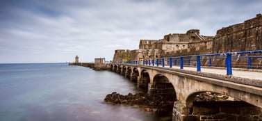 A long stone bridge leading to Castle Cornet along the Guernsey coastline, representing the stable and established structures for different business entities in Guernsey.